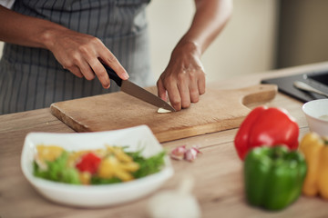 Close up of mixed race woman in apron standing in domestic kitchen and cutting garlic.