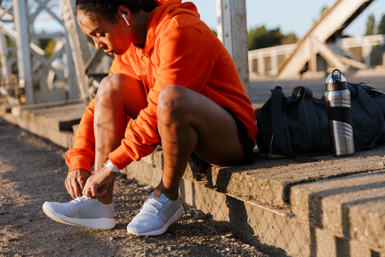 Photo of african american woman using earpods and tying shoelaces