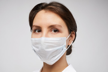 Head and shoulders portrait of female doctor wearing protective mask and looking at camera posing against white background