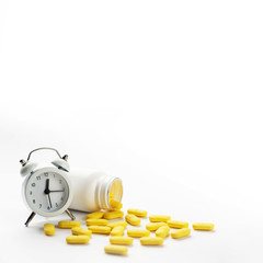 White alarm clock and spilled yellow pills against white background