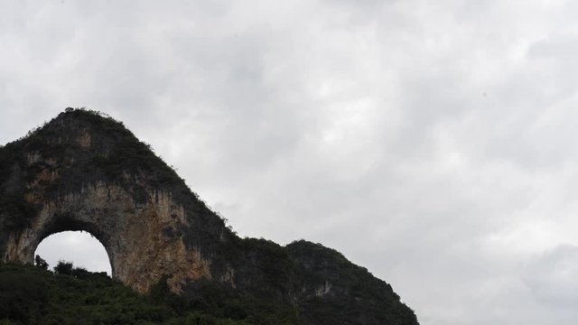 Wide shot time lapse panning left to see Moon Hill in Yangshuo, Guilin, China with white clouds moving across the sky.