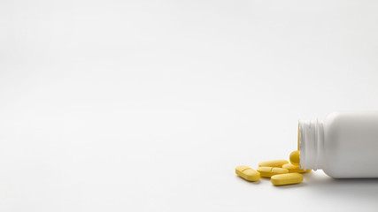 Yellow pills spilled from bottle isolated over white background