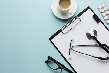 Overhead view of coffee cup and doctor's equipment on blue surface
