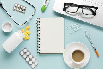 Healthcare supplies with notepad; cup of coffee and spectacles on laptop over table