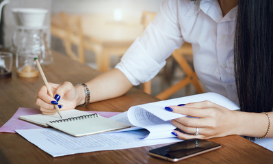 Young businesswoman reading information from paper and write on notebook