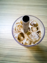 Close up on a tumbler glass full of iced coffee with a reusable metal drinking straw, on a wood restaurant table
