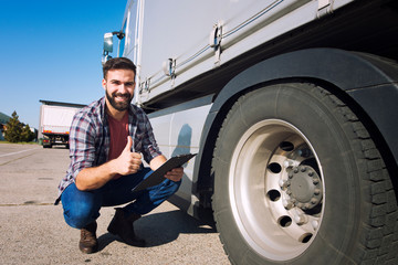 Truck driver with thumbs up inspecting tires condition and checking pressure. Truck preparation before ride. Transportation services.