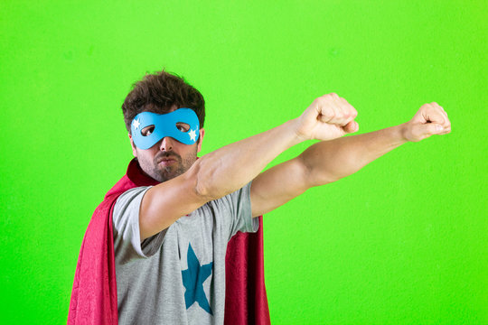 Superhero man with mask and red cape making flying gesture over green background
