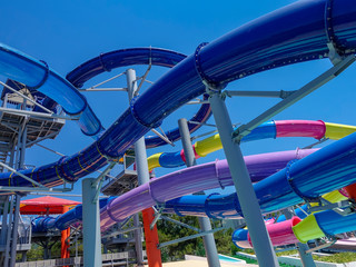 Colorful plastic water slides in waterpark against blue sky.