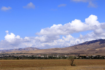Obraz premium Little city in valley, mountains and white clouds in the blue sky. Kaspi, Georgia.