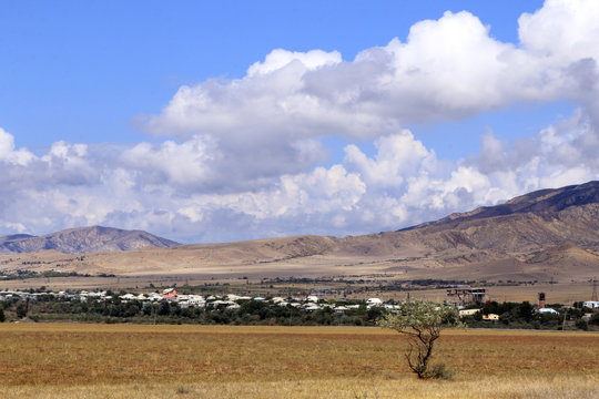 Little city in valley, mountains and white clouds in the blue sky. Kaspi, Georgia.