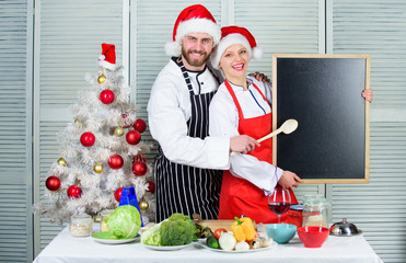 Cooking christmas meal. Christmas recipe concept. Menu for our family. Man and woman chef santa hat near christmas tree hold blackboard copy space. Couple read recipe together for christmas dinner