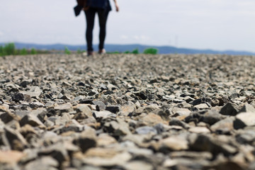 Road with sharp stones against the background of a girl walking in the distance.