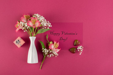 Valentine's day concept. Two chocolate hearts, a bouquet of alstroemeria in a white vase and write Happy Valentine's Day on a red paper background. Top view