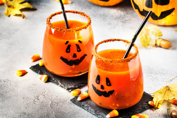 Halloween orange festive drink and pumpkin guards on gray autumn background with sweet corn, fallen...