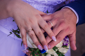 Fototapeta premium Hands of the bride and groom in wedding rings on a background of flowers.
