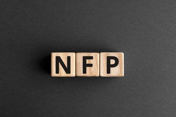 NFP - acronym from wooden blocks with letters, abbreviation NFP Nonfarm Payrolls key economic indicator or Natural Family Planning concept, gray background