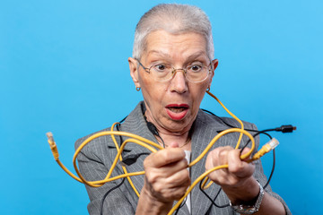Elderly woman looking confused while holding different types of electronic cables