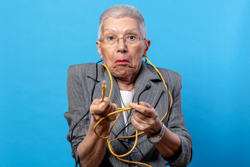 Elderly woman looking confused while holding different types of electronic cables