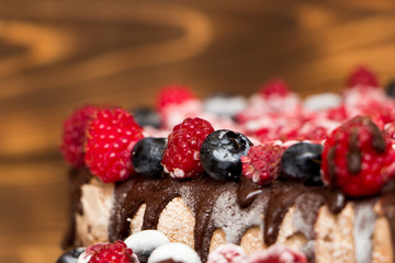 A close-up view of vegan chocolate cake covered with raspberries and blueberries, frozen in the refrigerator, on a table with blurred background. Copy space. Delicious healthy diet. Selective focus