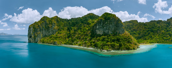 Fototapeta na wymiar Aerial panoramic drone view of uninhabited tropical island with towering mountains and rainforest jungle surrounded by blue ocean