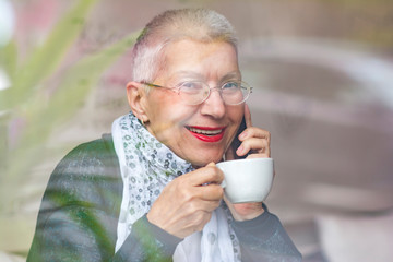 Cheerful old lady talking on her telephone at a coffee shop, looking joyous