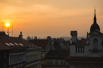 View of the roofs of historic buildings with red tiles during a bright sunset in Prague, Czech Republic.