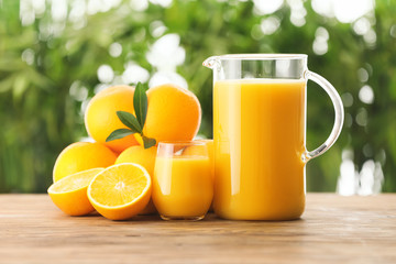 Glassware with fresh juice and oranges on table outdoors