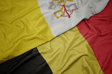 waving colorful flag of belgium and national flag of vatican city.