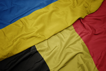 waving colorful flag of belgium and national flag of ukraine.