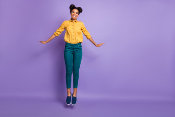 Full length photo of pretty dark skin lady jumping high flirty coquettish mood vacation time wear casual yellow shirt trousers isolated purple color background