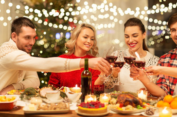 holidays and celebration concept - happy friends having christmas dinner at home, drinking red wine and clinking glasses