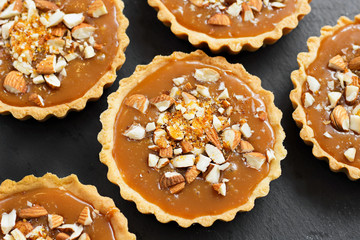 Shortcake sucre dough pastry caramel tartlets tart with caramel brittle, nuts, almonds, caramel crumbs on a black slate plate. Top view portioned dessert for celebration