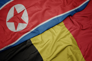 waving colorful flag of belgium and national flag of north korea.