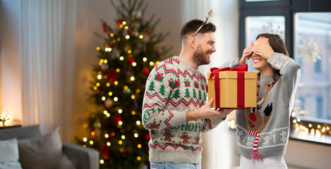 Obraz na płótnie Canvas people and holidays concept - portrait of happy couple with christmas gift at ugly sweater party