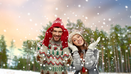christmas, clothes and holidays concept - portrait of happy couple in ugly sweaters over winter park background
