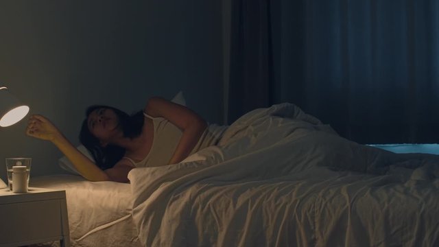 Beautiful Asian young woman sleeping cozily in her bedroom. Indian female hand turning off on light switch near bed in room at home in late night ready to sleep. Sweet dreams and relaxation concept.