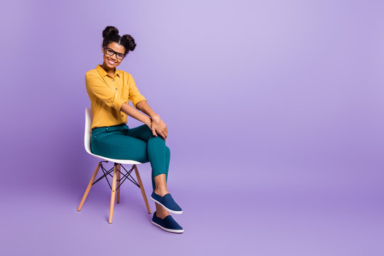 Full length photo of amazing dark skin lady sitting on chair looking positive listen employer question wear specs yellow shirt trousers isolated purple color background