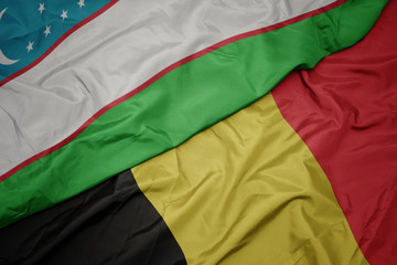 waving colorful flag of belgium and national flag of uzbekistan.