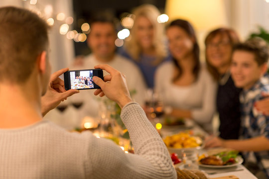 celebration, holidays and people concept - man with smartphone taking picture of family at dinner party