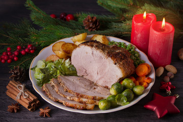 Roasted sliced ham on white plate, table with Christmas decorations. Dish for Christmas Eve. Winter season holidays food
