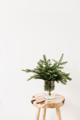 Bouquet made of fir branches on solid wooden stool on white background. Minimalistic Christmas composition.