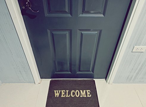 Welcome doormat in front of the wooden door dark green color.