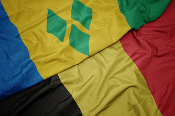 waving colorful flag of belgium and national flag of saint vincent and the grenadines.