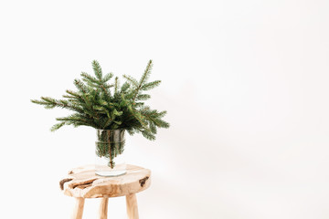 Bouquet made of fir branches on solid wooden stool on white background. Minimalistic Christmas composition.