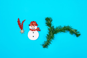 The concept is a symbol of the new year. A little white snow is located on a blue background, on which lies a sprig of green spruce, and a red-white shiny decoration in the form of a star.
