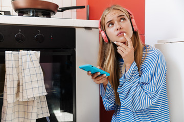 Image of confused girl using smartphone while cooking in oven at home