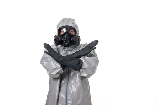 A man poses in a gray protective suit with a hood on his head with a yellow radiation sign, with a protective gas mask, posing while standing on a white background. Indicates stop sign. Isolated 