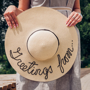 A Woman Holds In Her Hands A Large Round Straw Hat On The Street.