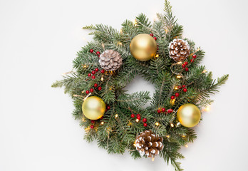 winter holidays, new year and decorations concept - wreath of fir branches with golden balls, pine cones and garland lights on white background